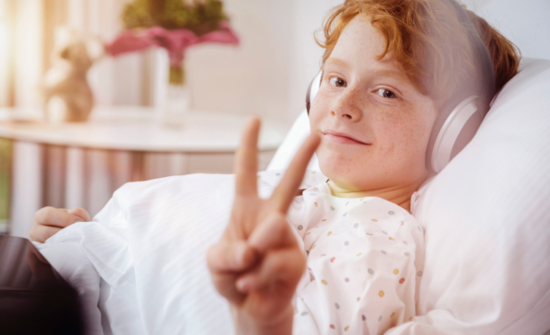 Bild eines lächelnden Jungen im Krankenhausbett, der Musik hört
